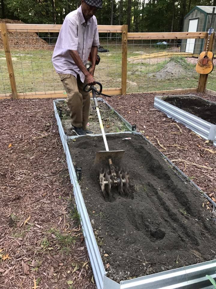 man tilling a garden bed by hand to prepare it to be seeded