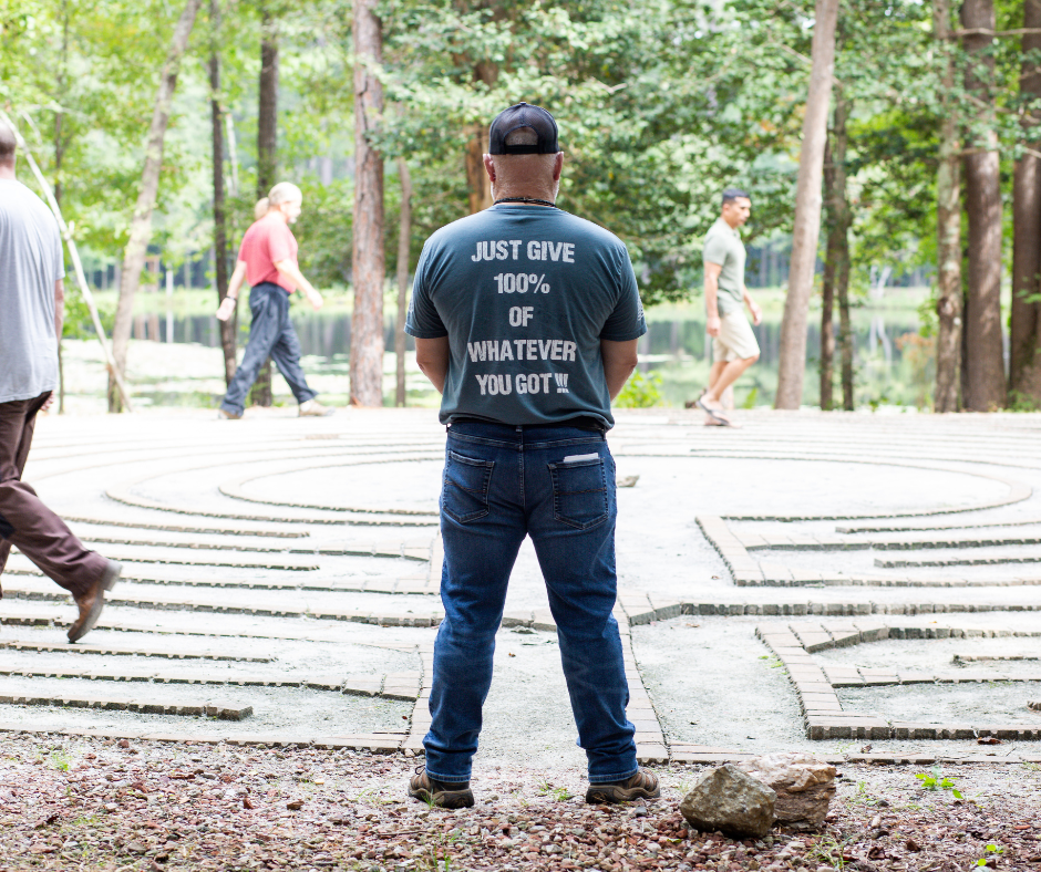 Man standing in front of a labyrinth in a park, shirt says “Just give 100% of whatever you got.”.