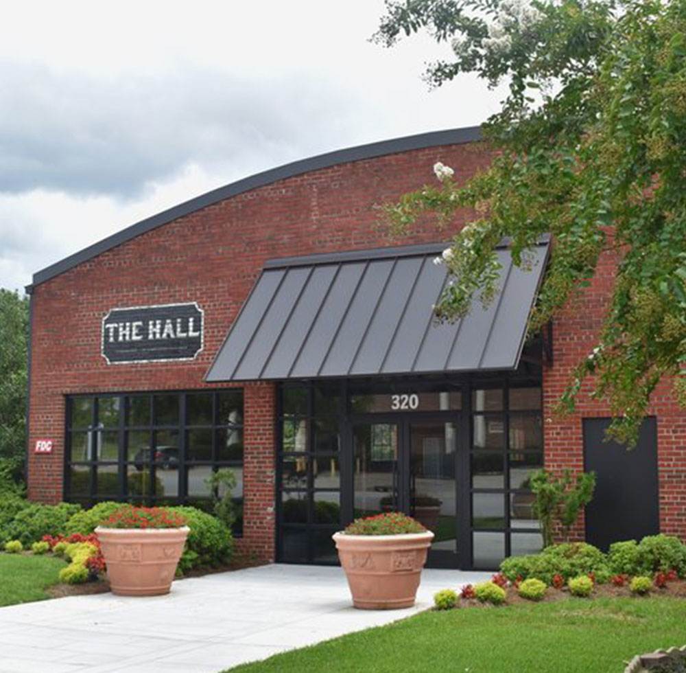 Red brick building with black awning, labeled The Hall, and two large planters by the entrance.