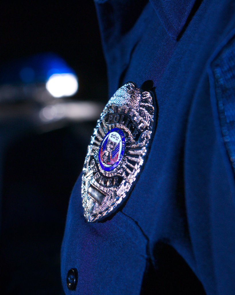 Close-up of a police officer’s badge on a dark blue uniform, with blurred light in the background.